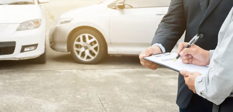 A man signing a car insurance claim following a car crash